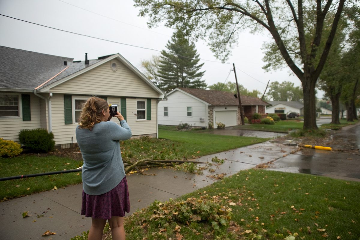 A homeowner photographing her house roof with a phone after a storm