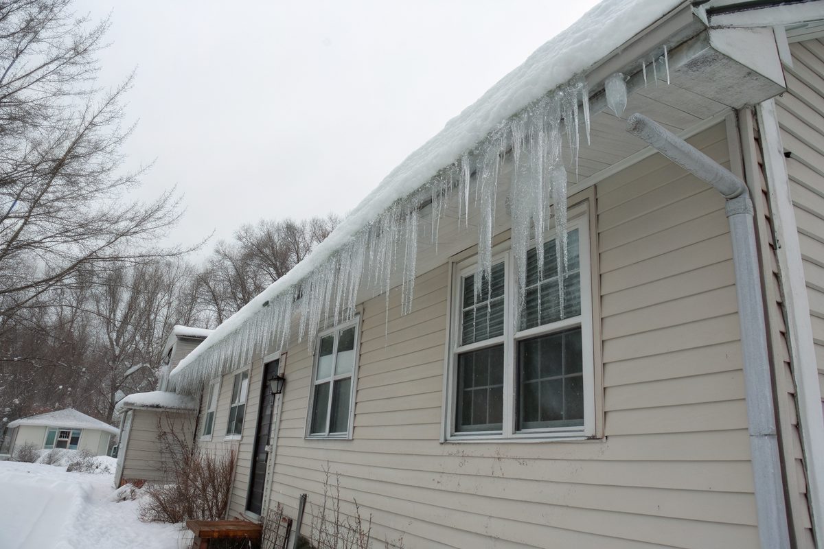 A thick ice dam and long icicles along the snowy eave of a one-story house